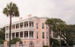 A large pink building with two balconies and palm trees.